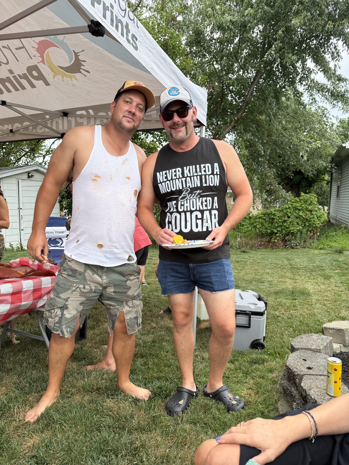 Two guys in tank tops loading up plates under the tent
